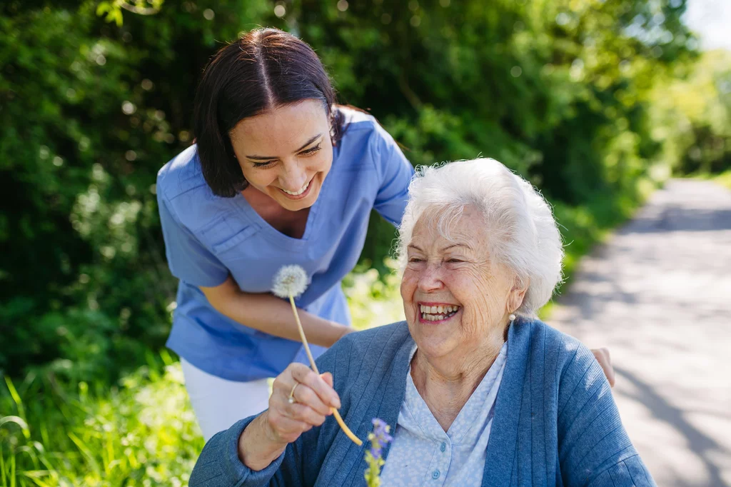 Female caregiver and senior woman in wheelchair holding dandelion