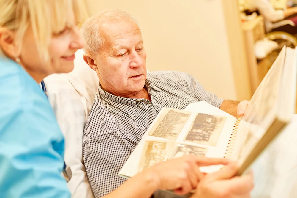 Caregiver and senior man reviewing photo album in a residential setting.